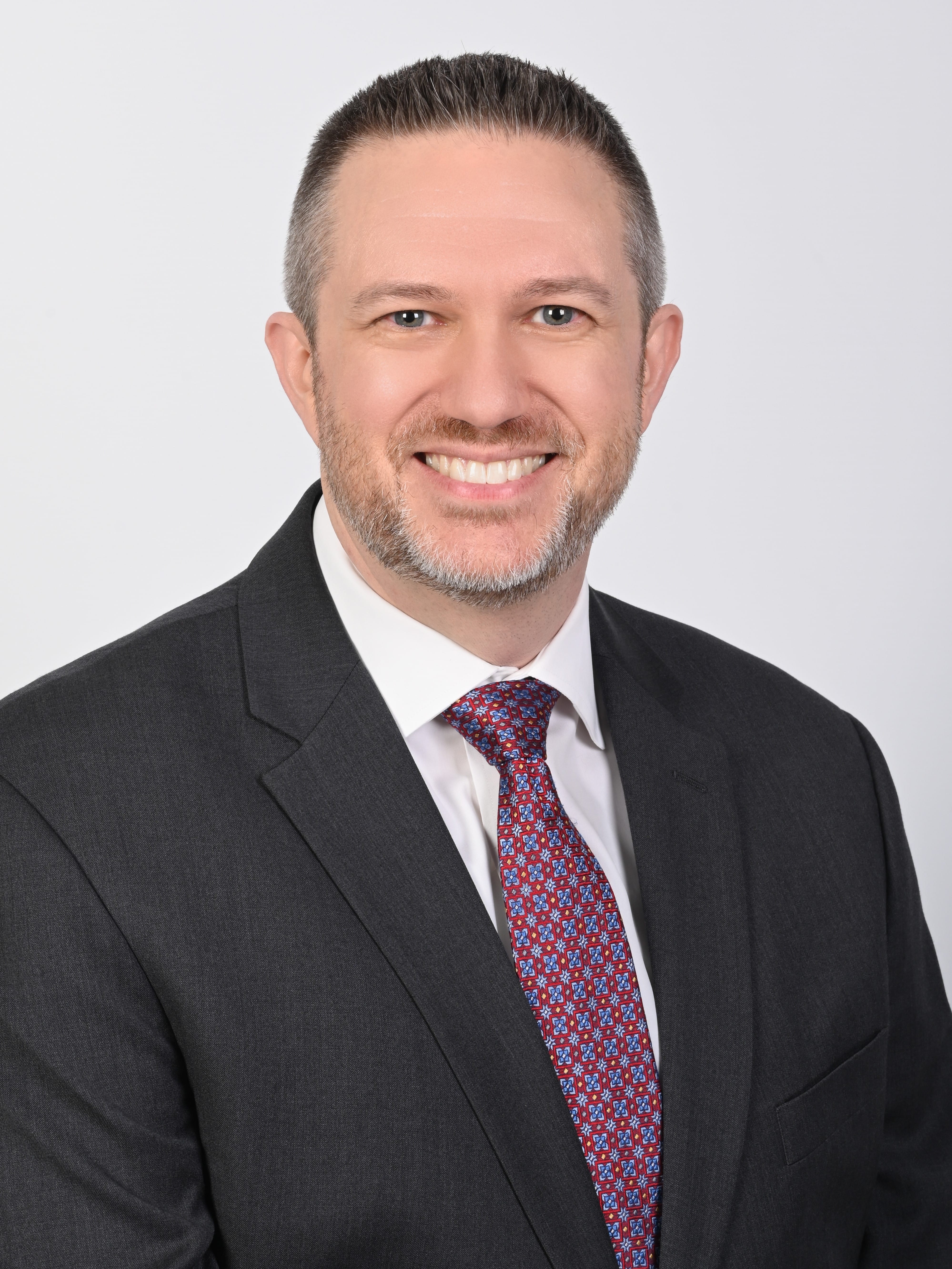 Brian Adams smiles for headshot photo wearing a suit and tie