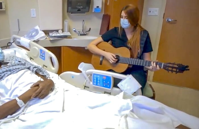 A music therapist plays guitar at the bedside of a hospital patient.