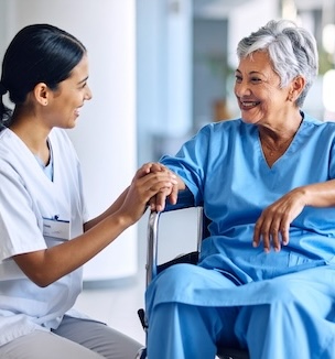 Thumbnail image of a female nurse squatting beside a wheelchair bound patient, holding her hand.