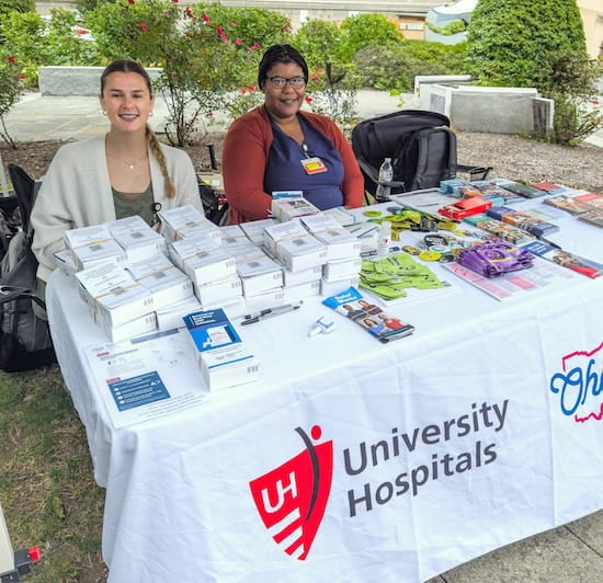 Two female pharmacists sit at a UH Emergency Medicine booth to distribute Narcan kits to the public.