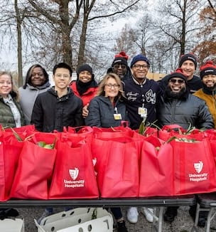 Thumbnail image of a group of smiling UH volunteers behind red bags full of food.